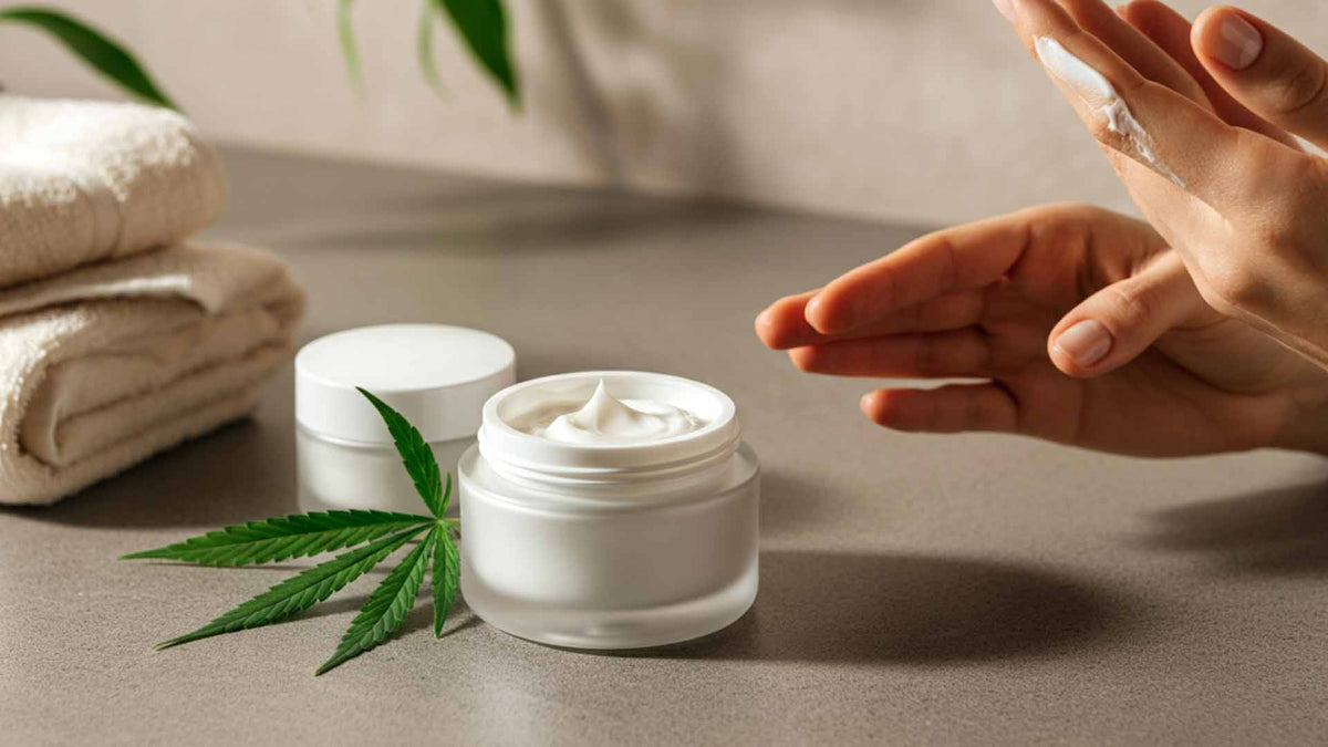 Nine Realms cannabis cream in a glass jar and a white lid on a grey stone surface with two hands nearby and towels