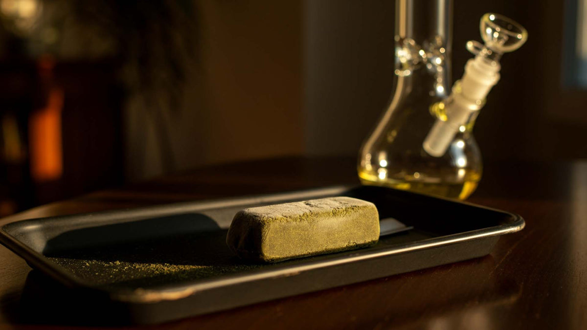 Nine Realms frozen hash block on a roling tray next to a bong