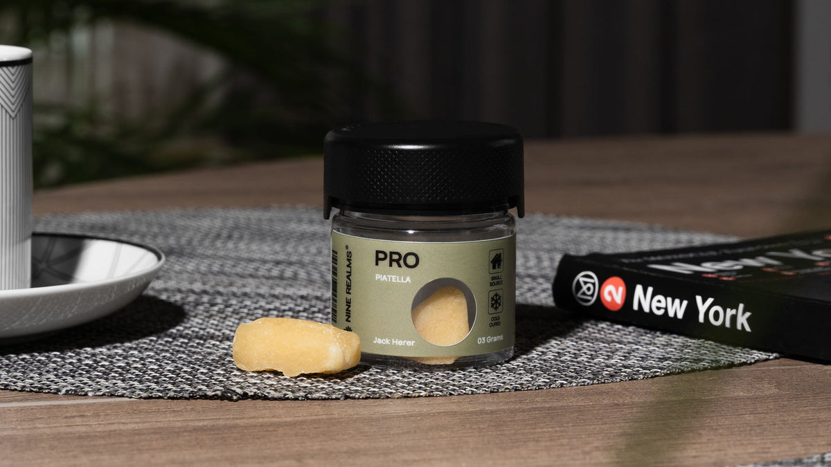 Nine Realms Piatella hash product in a green jar on a wooden table with a book next to it