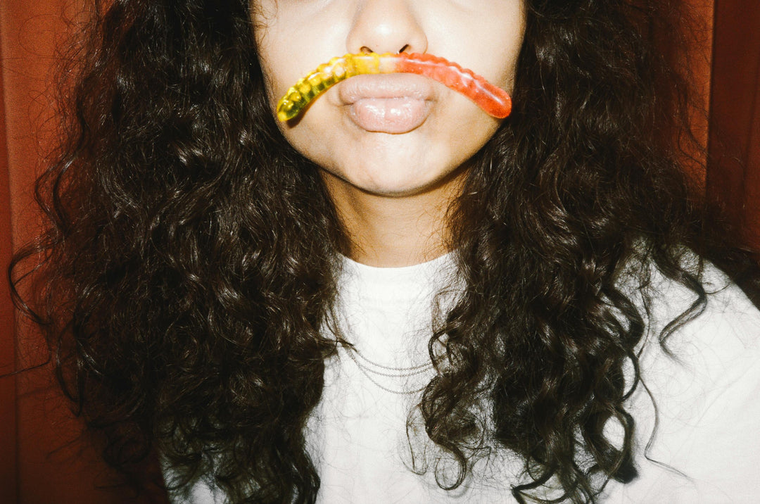 Woman holding a nine realms hhc gummy worm in between her lip and nose